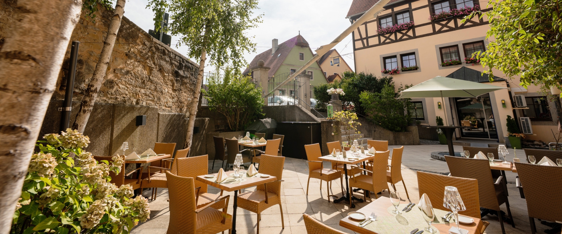 Sonnige Hotelterrasse des Prinzhotel Rothenburg mit gedeckten Tischen und Fachwerk im Hintergrund.